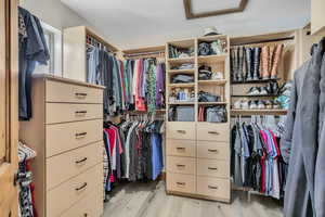 Walk in closet featuring attic access and light wood-style floors
