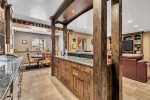 Kitchen featuring dark stone countertops, wood finish cabinets, stone tile flooring, open floor plan, and recessed lighting