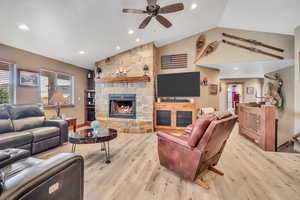 Living room featuring a ceiling fan, a fireplace, vaulted ceiling, recessed lighting, and light wood-type flooring