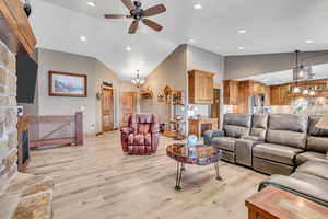 Living area featuring hanging lights, ceiling fan, light wood-type flooring, vaulted ceiling, and a stone fireplace