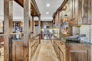 Kitchen featuring dark stone counters, stainless steel appliances, stone tile flooring, backsplash, and recessed lighting