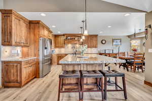 Kitchen with light stone counters, wood finish cabinetry, light wood finished floors, stainless steel refrigerator with ice dispenser, and a kitchen bar