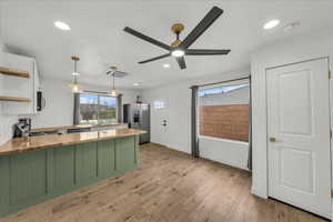 Dual tone kitchen with pendant lighting, open shelves, a peninsula, light wood-type flooring, and stainless steel refrigerator with ice dispenser