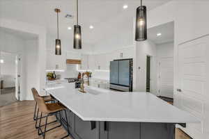 Two tone kitchen with decorative light fixtures, a large island with sink, a breakfast bar, two tone color scheme, and light wood finished floors