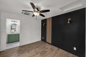 Unfurnished bedroom featuring wood finished floors, cooling unit, a ceiling fan, and ensuite bathroom