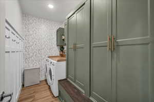 Laundry area with wallpapered walls, light wood-style flooring, cabinet space, and separate washer and dryer