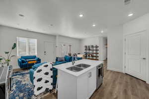 Kitchen featuring white cabinetry, an island with sink, open floor plan, wood finished floors, and recessed lighting