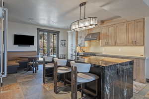 Kitchen featuring a breakfast bar area, stone tile floors, decorative light fixtures, and dark stone counters