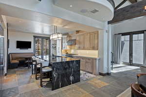 Kitchen featuring french doors, a breakfast bar area, stone tile flooring, and a center island with sink