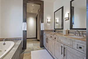 Full bath featuring double vanity, stone tile floors, a tub with jets, and recessed lighting
