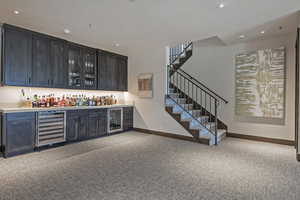 Indoor dry bar featuring light colored carpet, glass fronted cabinets, beverage cooler, and recessed lighting