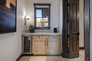 Indoor wet bar featuring wine cooler, light countertops, and light wood finish cabinets