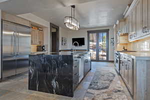 Kitchen with an island with sink, french doors, high quality appliances, pendant lighting, and exhaust hood