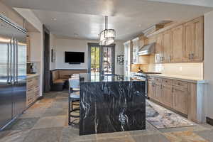 Kitchen with a center island with sink, high quality appliances, light wood finish cabinets, a breakfast bar area, and stone tile floors
