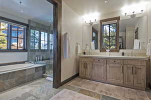 Full bathroom with stone tile flooring, double vanity, a garden tub, and a stall shower