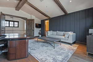 Living area with wood finished floors, a decorative wall, and lofted ceiling with beams