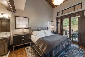 Bedroom with access to exterior, dark wood-style floors, and vaulted ceiling