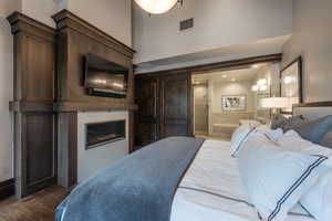 Bedroom with a high ceiling, wood finished floors, and a glass covered fireplace