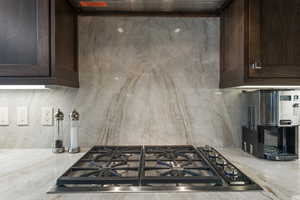 Kitchen view of dark wood finish cabinetry, stainless steel gas stovetop, light stone countertops, and exhaust hood