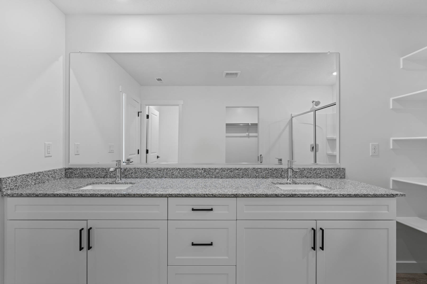 Dual sink vanity featuring light-colored stone-finish countertops and white cabinetry with matte black hardware