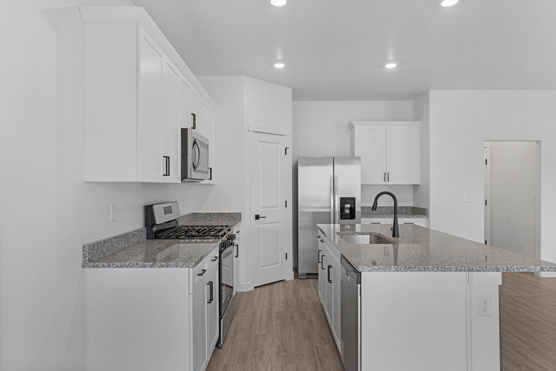 Modern kitchen featuring white cabinetry, stone countertops, stainless steel appliances, a center island with sink, and wood-finish flooring
