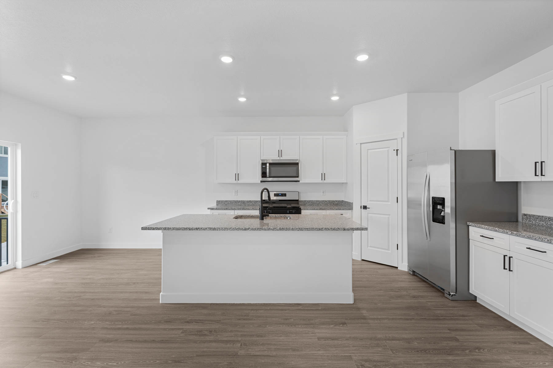 Modern kitchen featuring white cabinetry, granite countertops, a central island with an integrated sink, stainless steel appliances, and recessed lighting