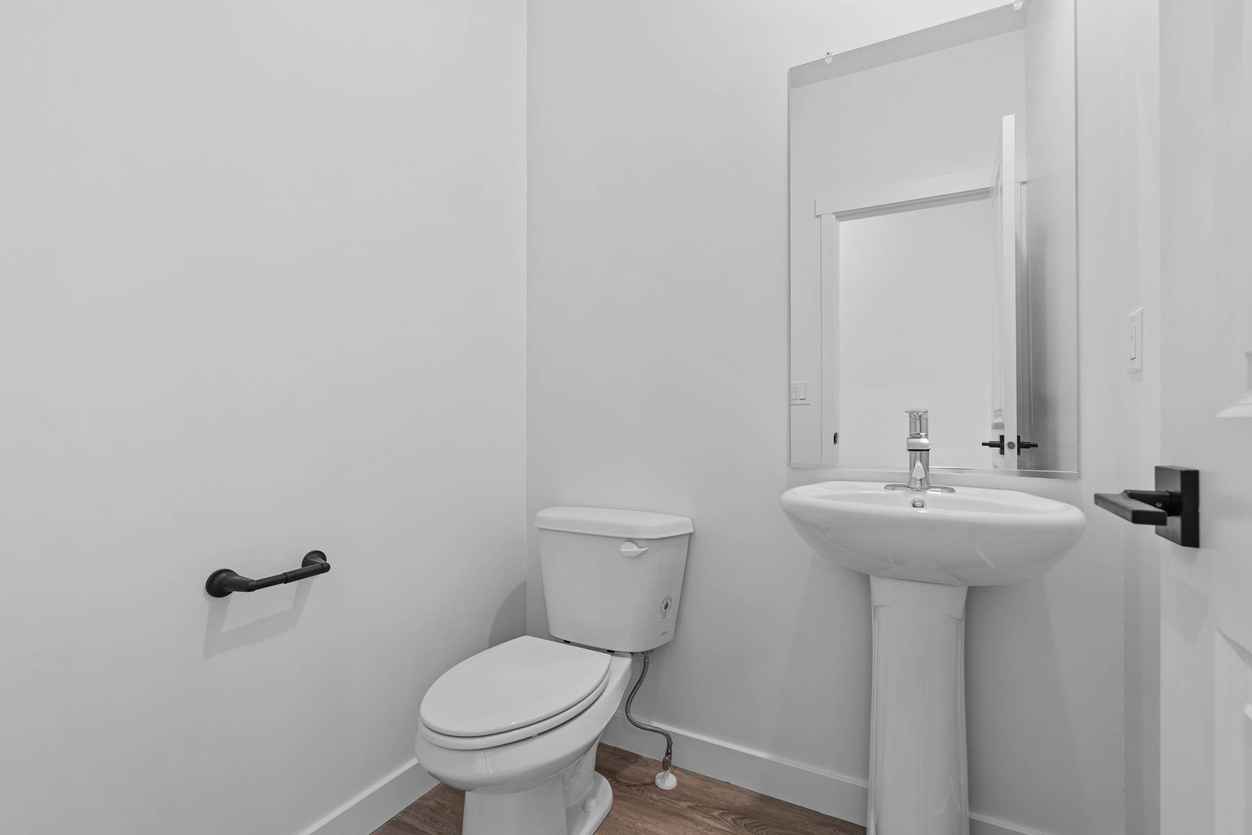 Pedestal sink with chrome faucet, wall-mounted mirror, and wood-finish flooring