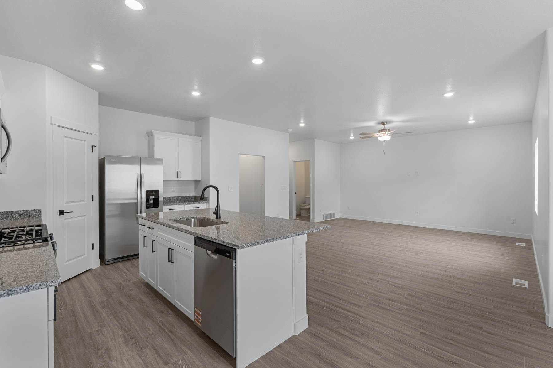 Open-concept living space featuring a kitchen island with sink and stainless steel dishwasher, wood-finish flooring, recessed lighting, and a ceiling fan
