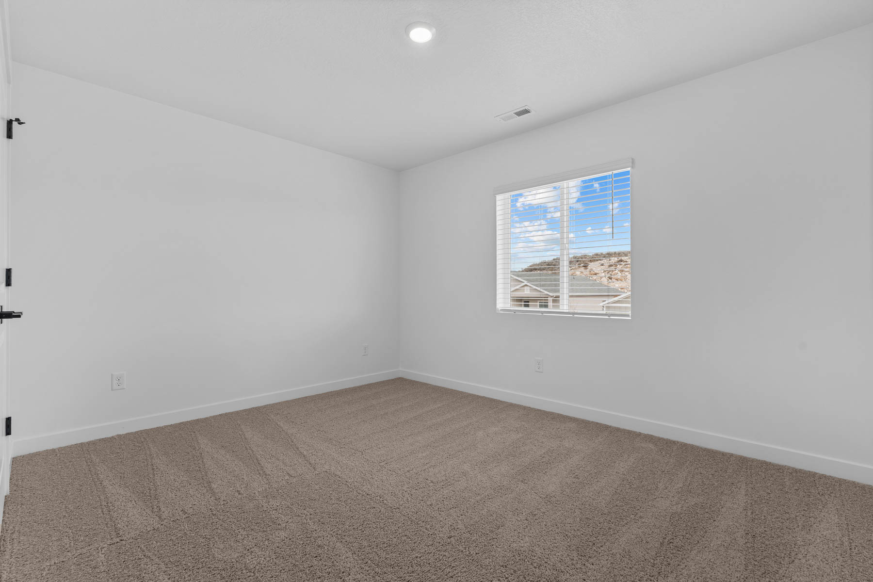 Neutral-toned carpeting enhances this bright room with white walls and a single window featuring blinds