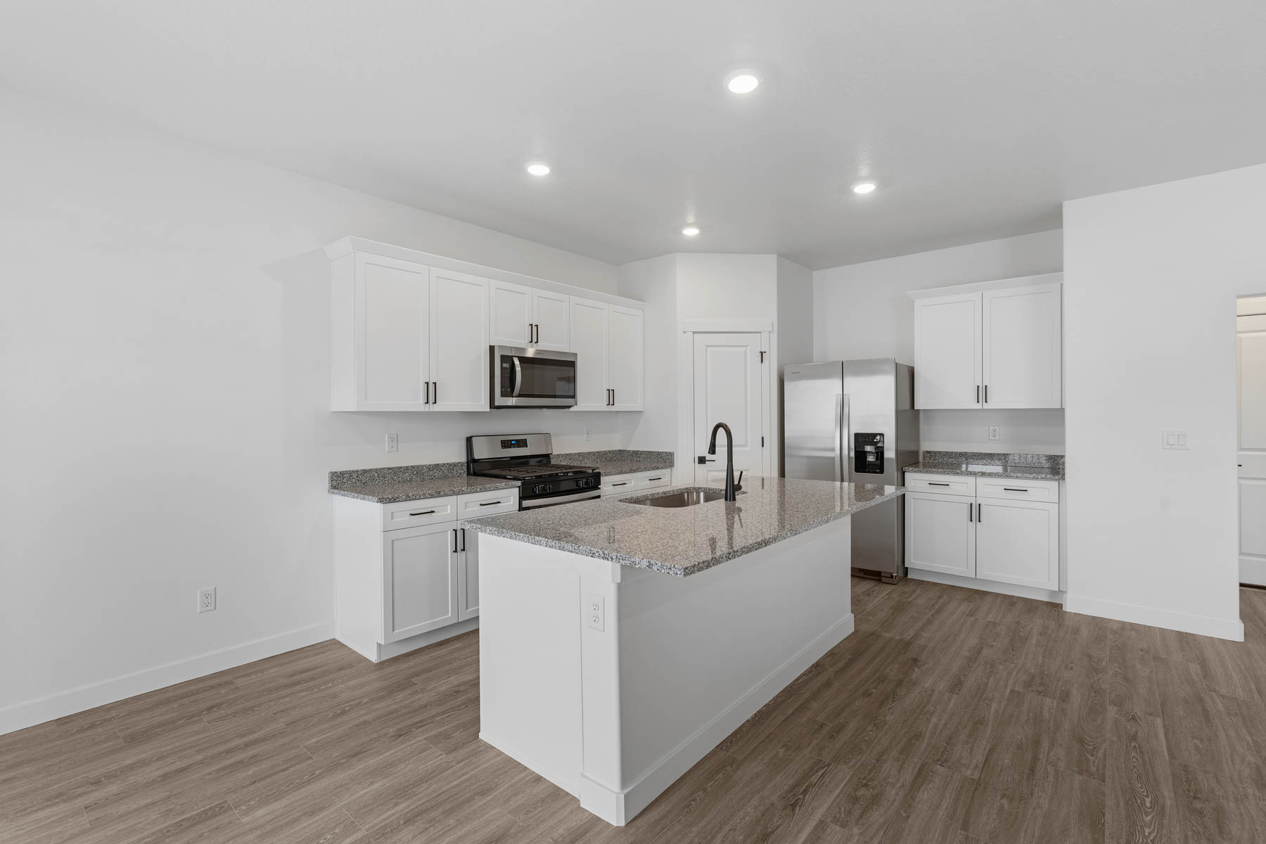 Modern kitchen featuring white cabinetry, granite countertops, stainless steel appliances, a center island with sink, and wood-finish flooring