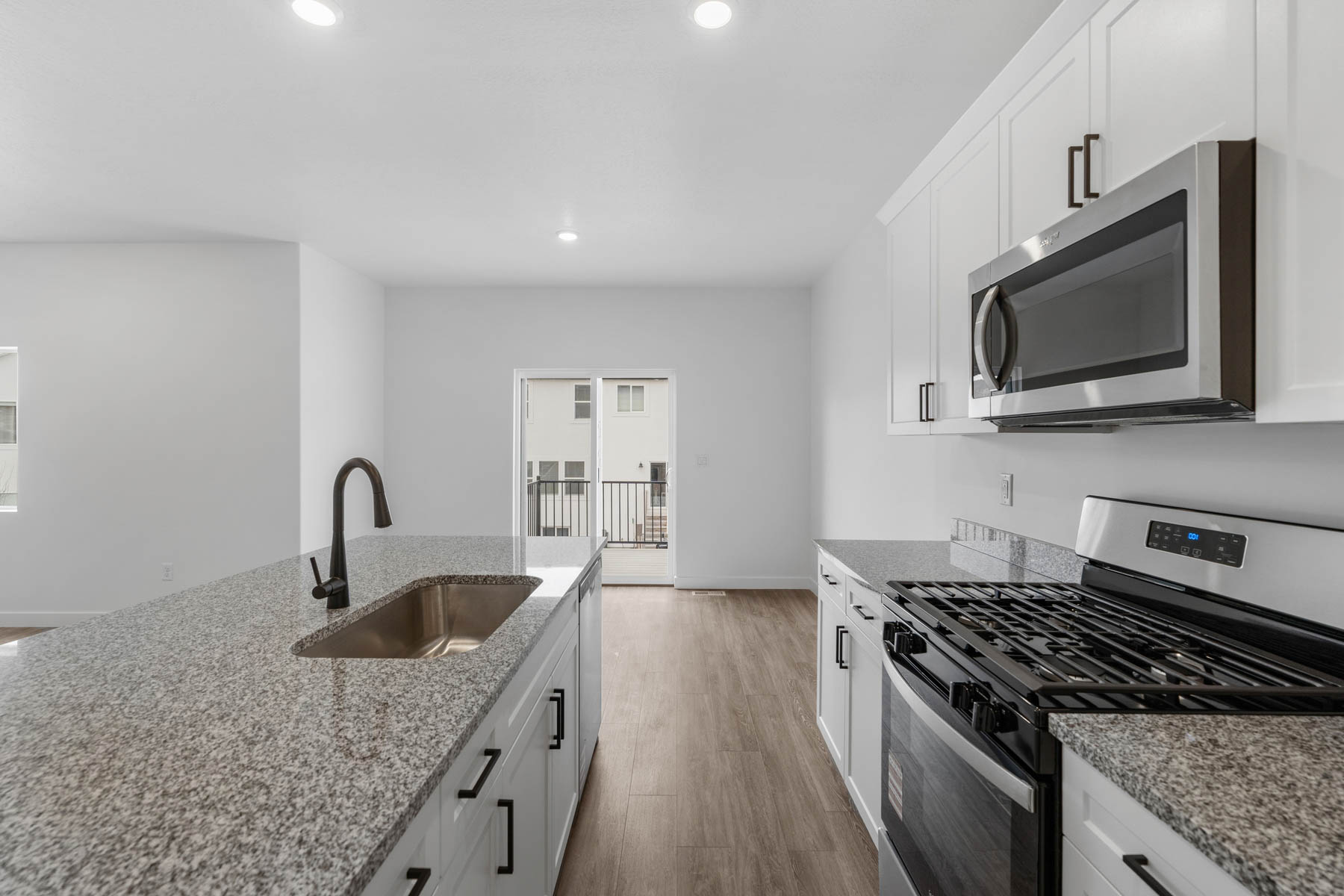 Modern kitchen featuring white cabinetry, granite-style countertops, stainless steel appliances, and wood-finish flooring