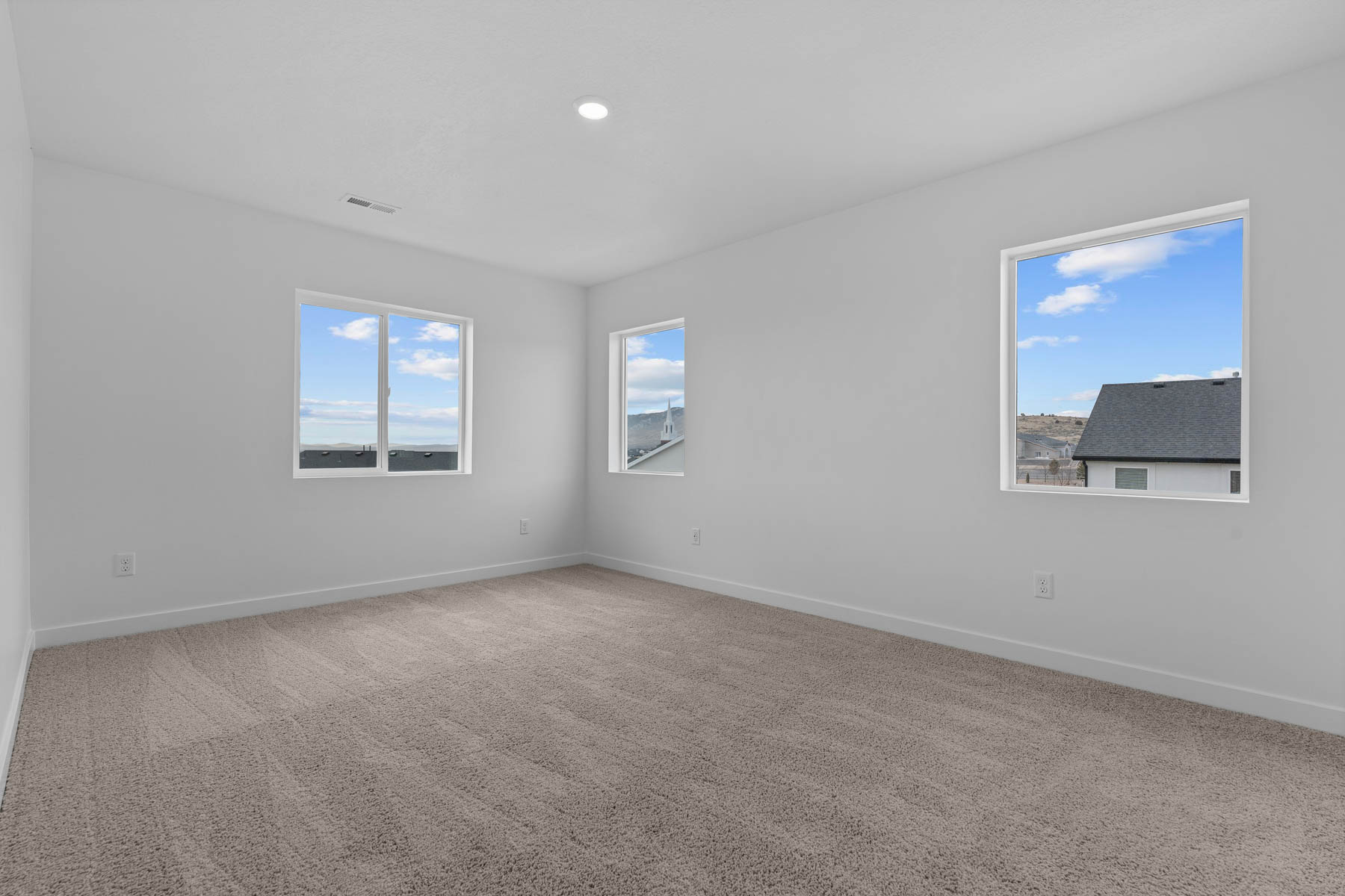 Spacious room featuring neutral carpeting, white walls, multiple windows, and a recessed ceiling light