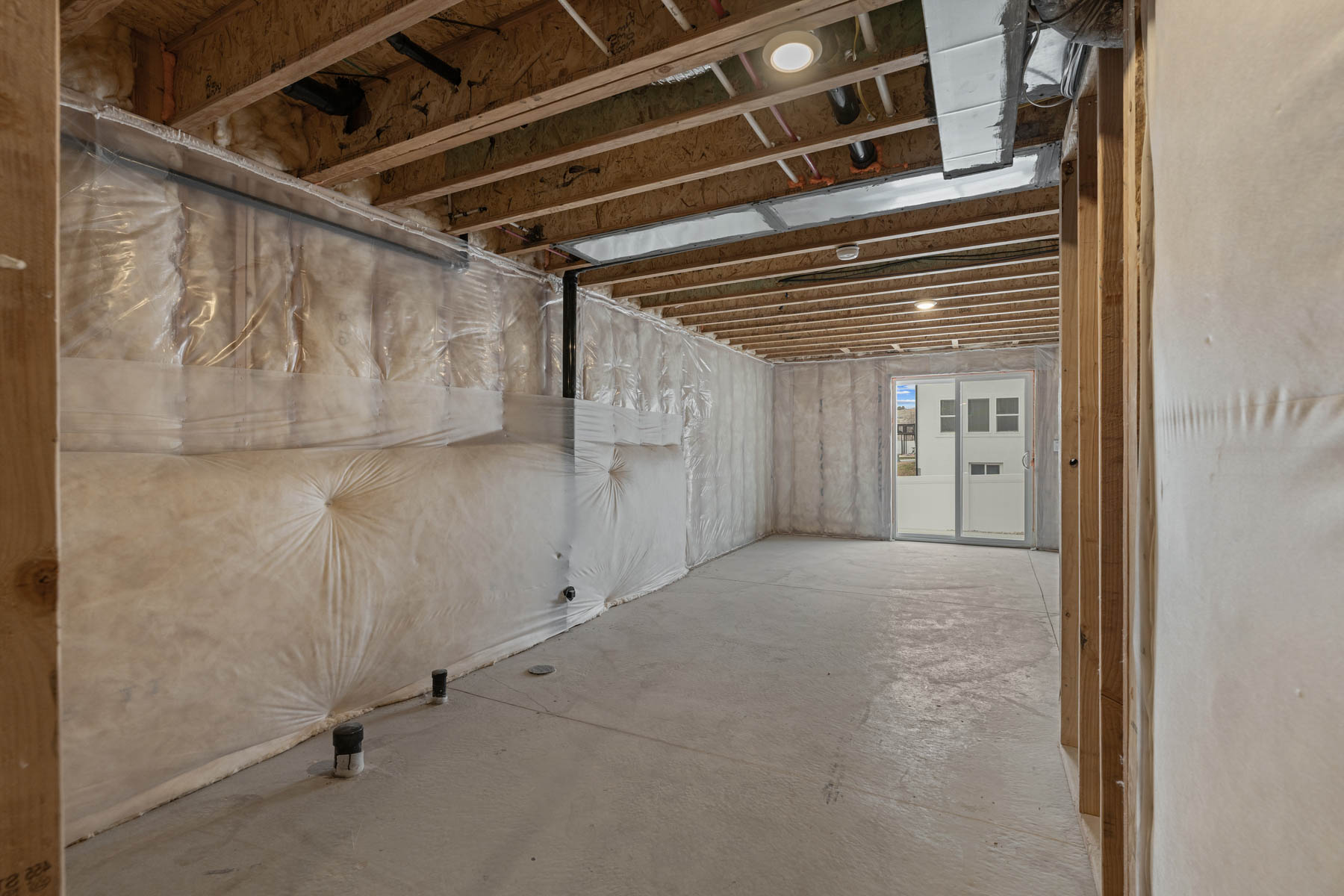 Unfinished basement featuring exposed wood joists, concrete flooring, and insulated walls