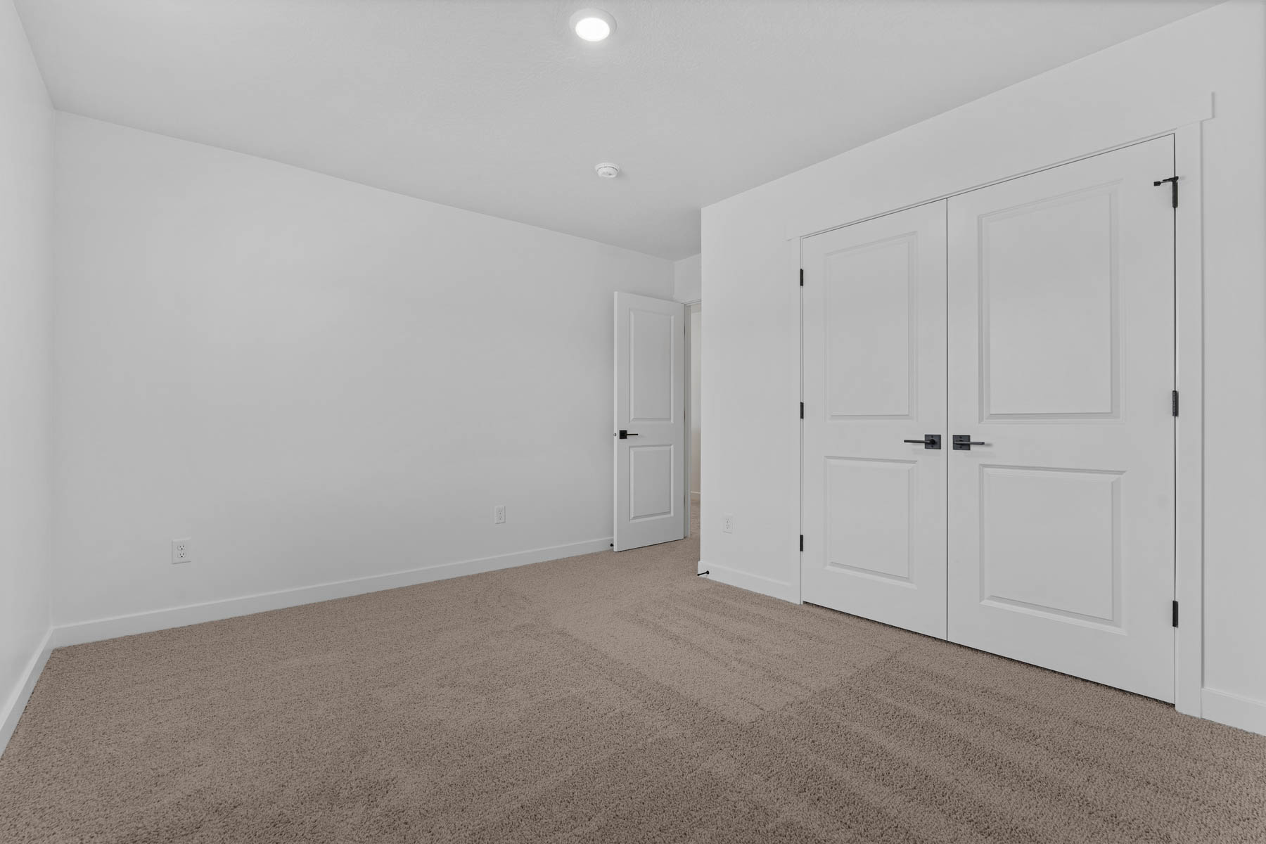 Spacious interior room with neutral-toned carpeting, white walls, and bright overhead lighting