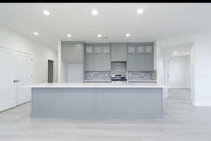 Kitchen with gray cabinetry, a large island, recessed lighting, light wood finished floors, and decorative backsplash