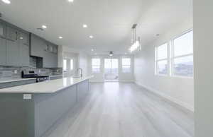 Kitchen with gray cabinets, stainless steel range with gas cooktop, a spacious island, hanging light fixtures, and tasteful backsplash