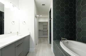 Bathroom featuring a bath, a walk in closet, double vanity, and light wood-style floors