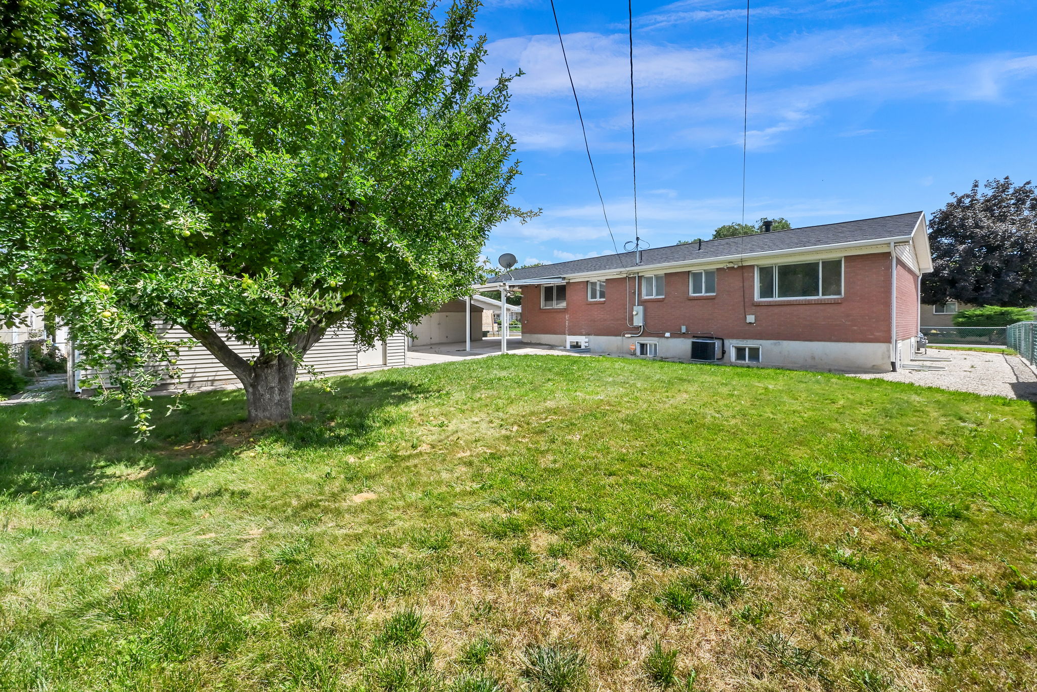 Expansive grassy yard area with a mature shade tree and a red brick exterior.
