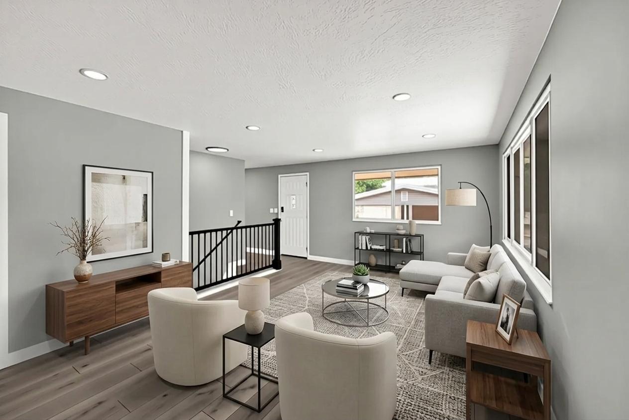 Open-concept living area featuring recessed lighting, light wood-finish flooring, and a contemporary black metal staircase railing. Virtually staged to illustrate the home's potential