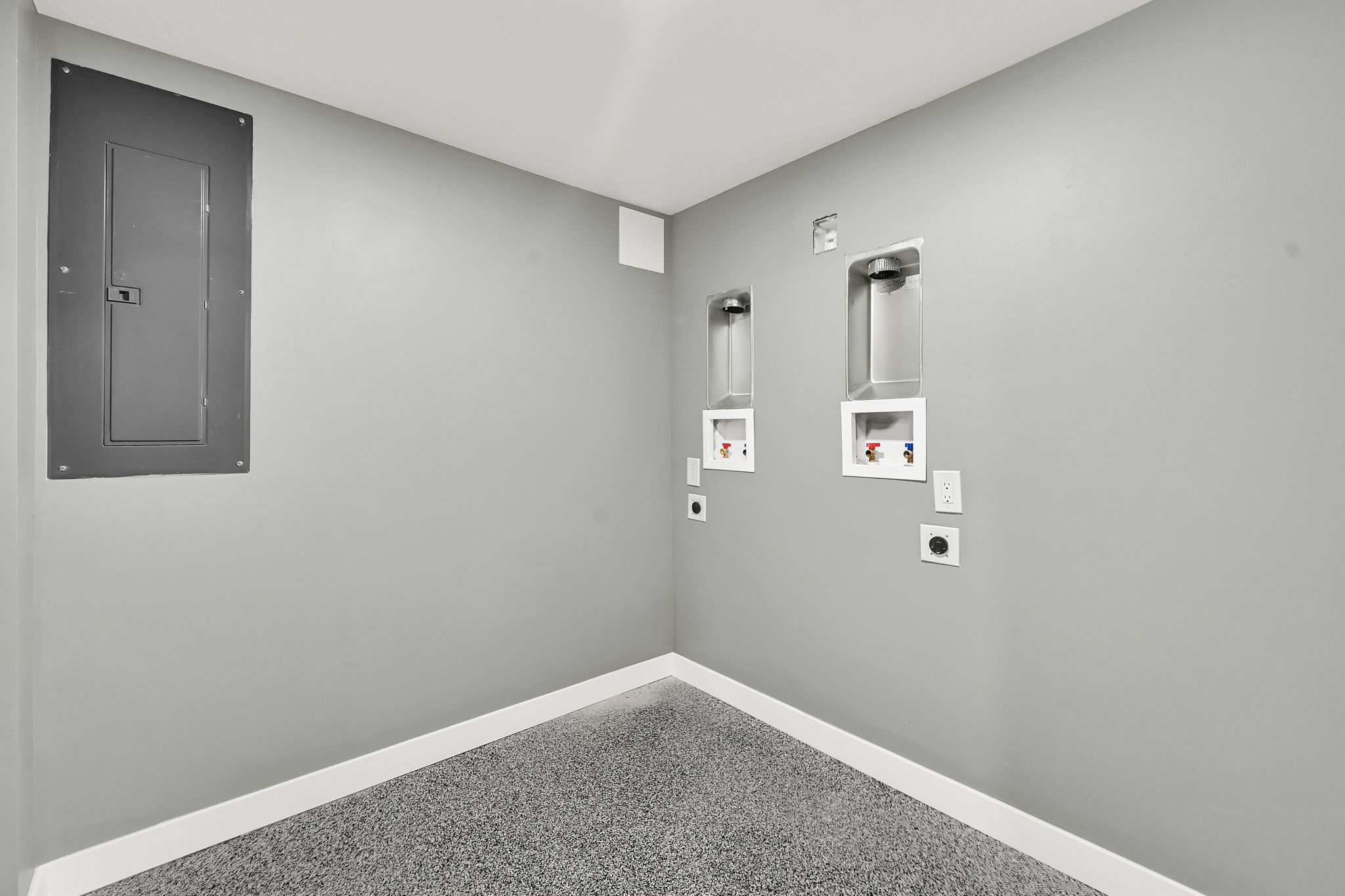 Dedicated laundry area featuring a durable epoxy-coated concrete floor, white baseboards, and pre-installed hookups for two stackable washer and dryers.