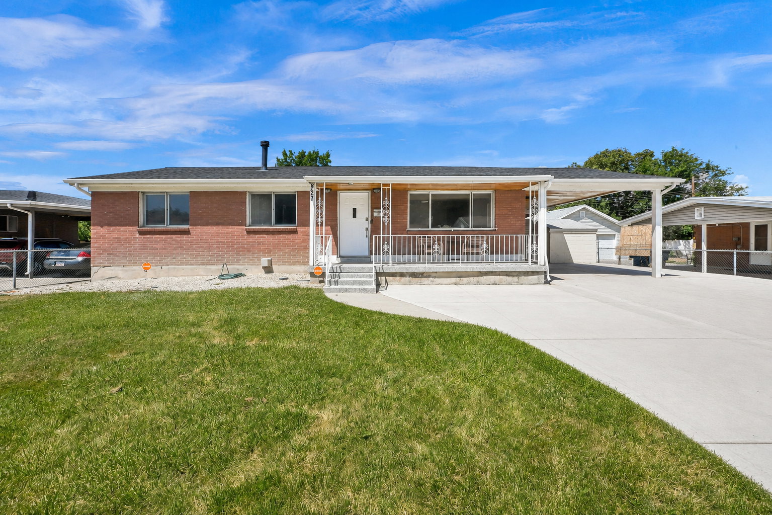 Red brick exterior with a front porch, concrete driveway, and covered carport