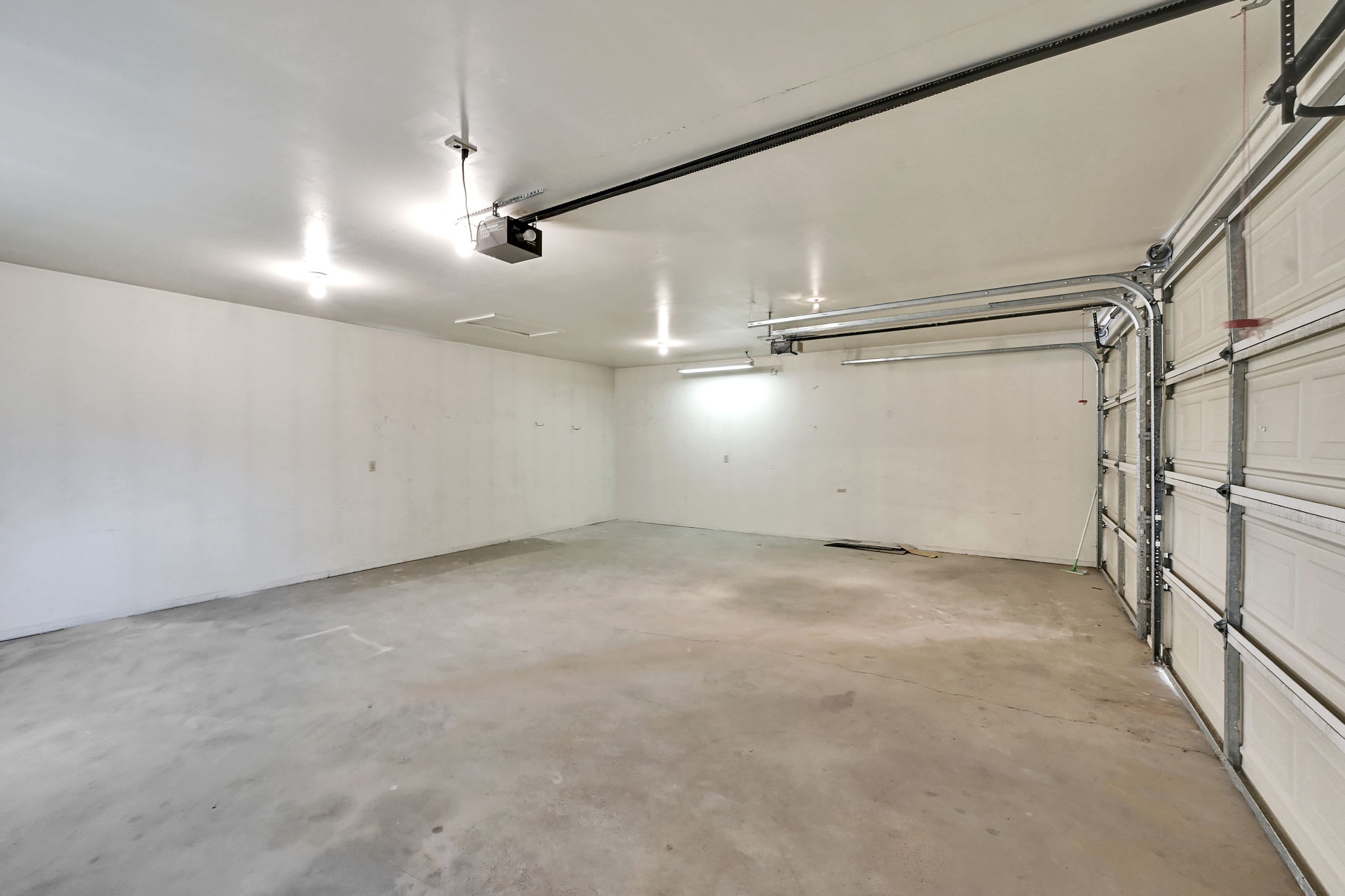 Spacious 3 car garage featuring a concrete floor, white interior walls, overhead lighting, and an automatic garage door opener.