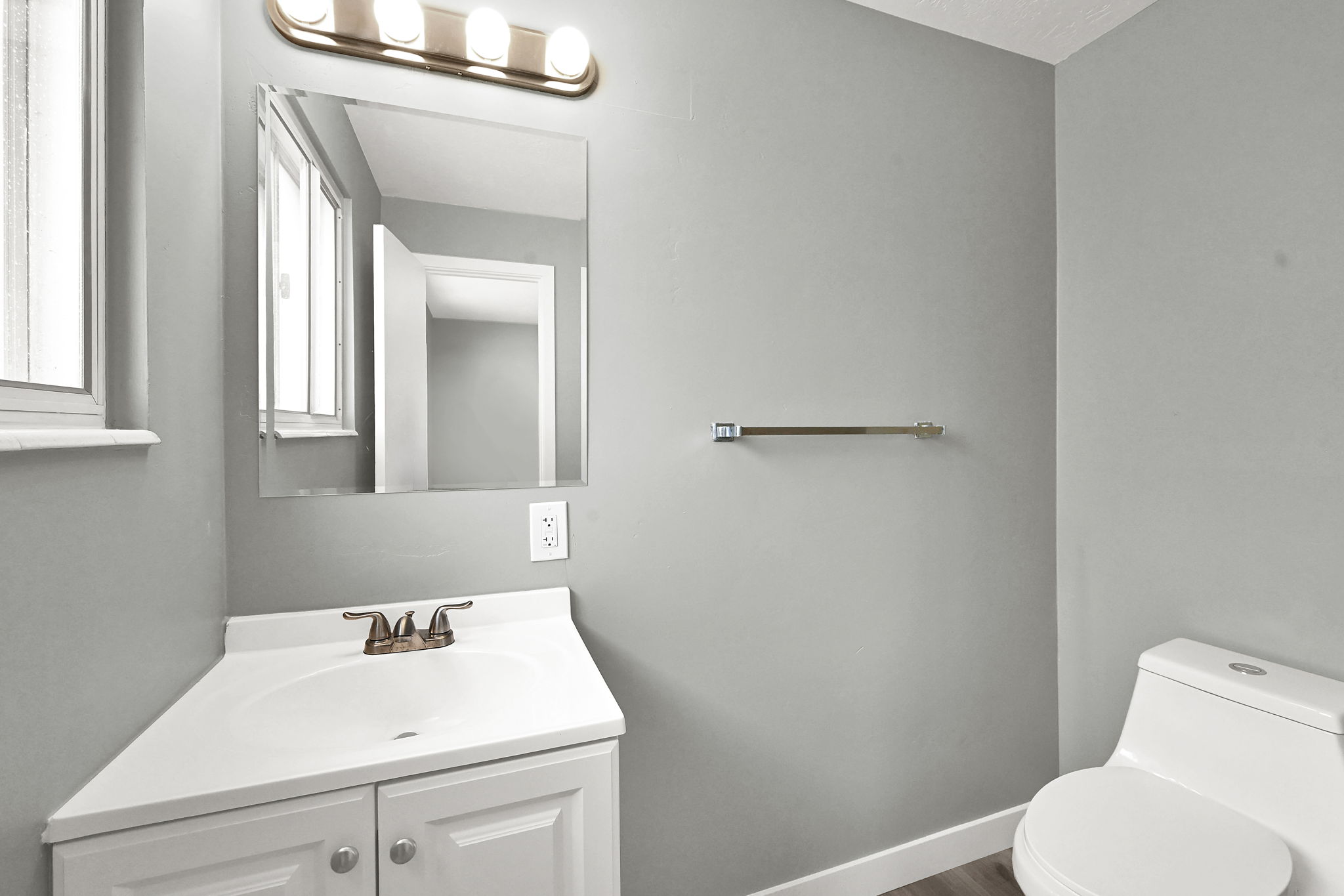 White corner vanity with an integrated sink, brushed brass faucet, and a rectangular mirror.