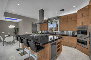 Kitchen with a breakfast bar area, a center island with sink, decorative backsplash, double oven, and dark stone counters