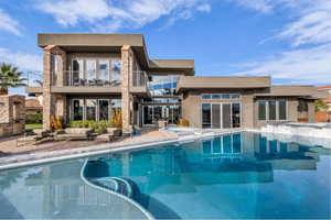 Rear view of property with a balcony, a pool with connected hot tub, stone siding, and stucco siding