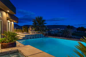 Pool at twilight with an outdoor pool, a hot tub, a mountain view, and a patio
