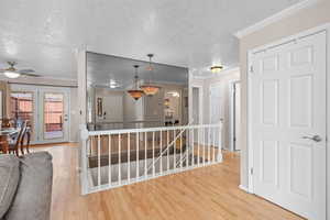 Hallway with ornamental molding, an upstairs landing, light wood finished floors, and a textured ceiling