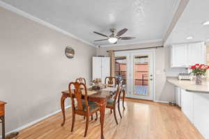 Dining room with a textured ceiling, light wood-style flooring, a ceiling fan, and ornamental molding