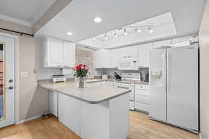 Kitchen featuring white appliances, white cabinetry, light wood-type flooring, a peninsula,