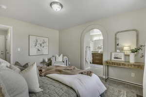 Carpeted bedroom featuring ensuite bath and arched walkways